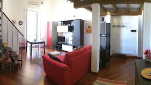 A spacious living area with a red sofa, wooden flooring, and a kitchen in the background. - Elegante App.to in Centro (Palermo)