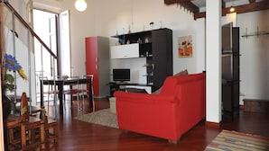 A modern living room with a red sofa, wooden flooring, and a dining area with a table and chairs. - Elegante App.to in Centro (Palermo)
