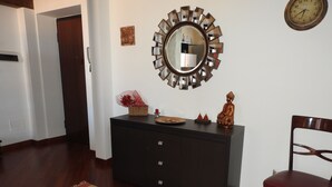 A room with a dark wooden cabinet, a mirror with a sunburst frame, a Buddha statue, and a red chair. - Elegante App.to in Centro (Palermo)