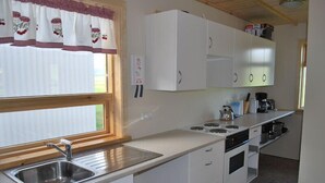 A compact kitchen with white cabinets, a stainless steel sink, a stove, and a coffee maker. - Thurranes guesthouses (Budardalur)