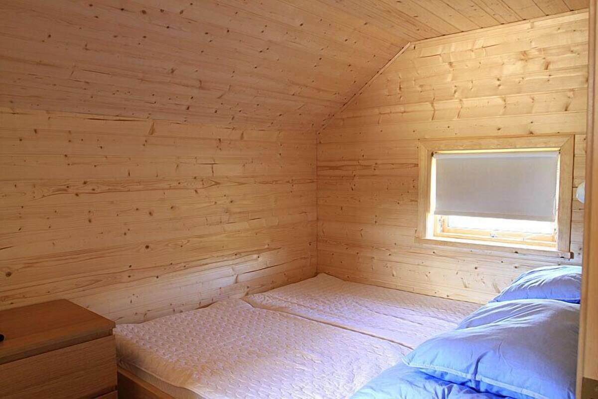 Une petite pièce aux murs lambrissés, avec un lit simple, une fenêtre et une table de chevet.