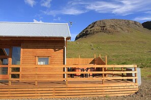Une cabane en bois avec un toit en métal, une terrasse avec des chaises et une vue sur une colline rocheuse.