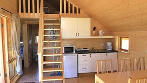 A wooden cabin interior with a kitchen, dining area, and a loft bedroom with a wooden ladder. - Thurranes guesthouses (Budardalur)