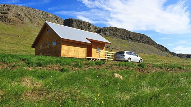 A wooden cabin with a metal roof, a car parked in front, and a mountainous backdrop. - Thurranes guesthouses (Budardalur)