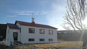 A white building with a red roof, a wooden fence, and a barren landscape. - Thorbrandsstadir Farm Holidays (Vopnafjordur)