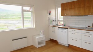 A kitchen with white cabinets, a wooden countertop, and a view of the countryside through large windows. - Thorbrandsstadir Farm Holidays (Vopnafjordur)