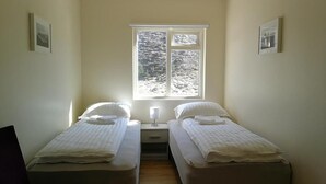 A room with two single beds, a nightstand, a window with a view of a rocky landscape, and framed pictures on the walls. - Thorbrandsstadir Farm Holidays (Vopnafjordur)