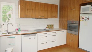 A modern kitchen with wooden cabinets, a stainless steel sink, a dishwasher, and a built-in oven. - Thorbrandsstadir Farm Holidays (Vopnafjordur)
