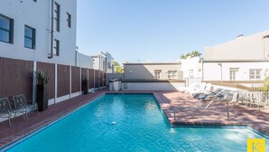 Una piscina con sillas de descanso, una valla de madera y un edificio con varias ventanas.