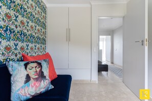 A modern living room with a dark blue sofa, a vibrant patterned wall, and a view into the adjacent bedroom. - 207 De Waterkant Piazza (Cape Town)