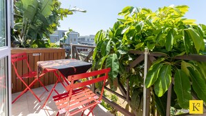 Un patio al aire libre con una mesa y sillas, rodeado de exuberante vegetación y vistas a edificios en el fondo.