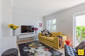 Een woonkamer met een bank, een televisie, een salontafel en een vloerkleed met bloemenmotief.