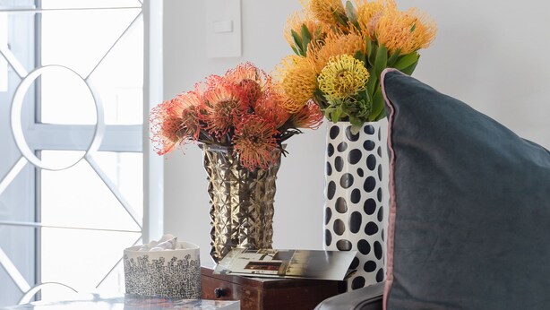 A wooden side table with a vase of flowers, a stack of books, and a decorative item. - 209 De Waterkant Piazza (Cape Town)