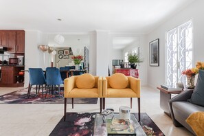 A modern living room with a sofa, a coffee table, and a dining area with chairs. - 209 De Waterkant Piazza (Cape Town)