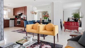 A modern living room with a sofa, coffee table, and a red dresser. There is a kitchen in the background with wooden cabinets and a dining area. - 209 De Waterkant Piazza (Cape Town)