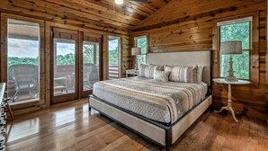 A spacious bedroom with a large bed, wooden walls, and a balcony with a view of the outdoors. - Majestic Sunrise- Pet Friendly | Screened Porch | Hot Tub (Blue Ridge)