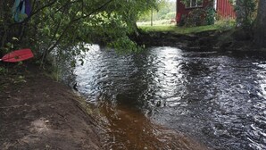 A river with a wooden dock and a red chair on the bank. - Lins B&B (Älvsered)