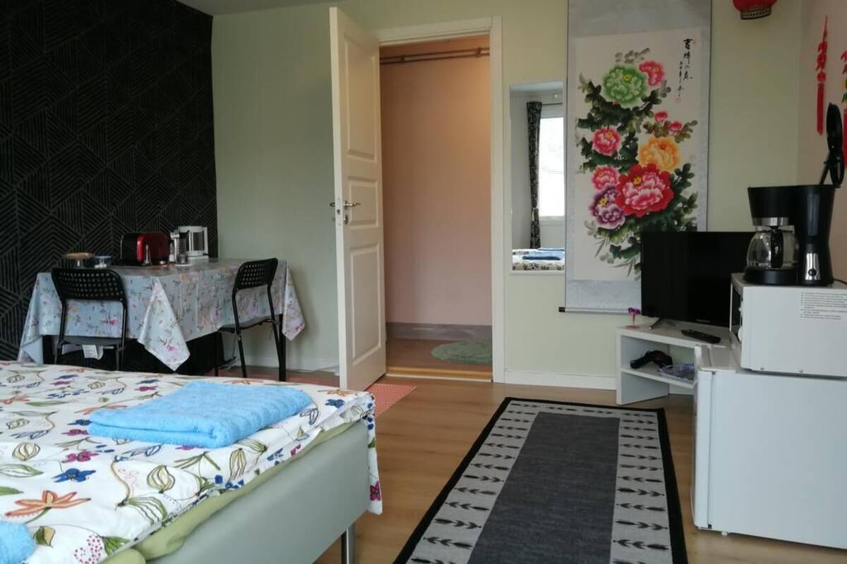 Ein Zimmer mit einem Bett, einem Tisch mit Stühlen, einem Kühlschrank und einem Wandbild mit floralem Dekor.