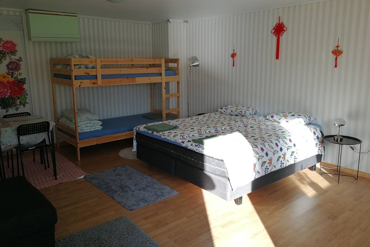 Ein Zimmer mit einem Etagenbett, einem Schreibtisch mit Stuhl, einem kleinen Tisch und einer Lampe.