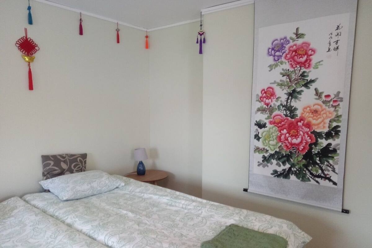 Ein ordentlich eingerichtetes Schlafzimmer mit Bett, Kissen, einem kleinen Nachttisch, einer Lampe und einer Wanddekoration.