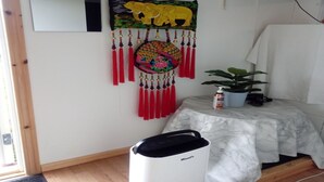 A room with a bed, a wall-mounted mirror, a decorative hanging with an elephant design, a trash bin, and a potted plant. - Lins B&B (Älvsered)
