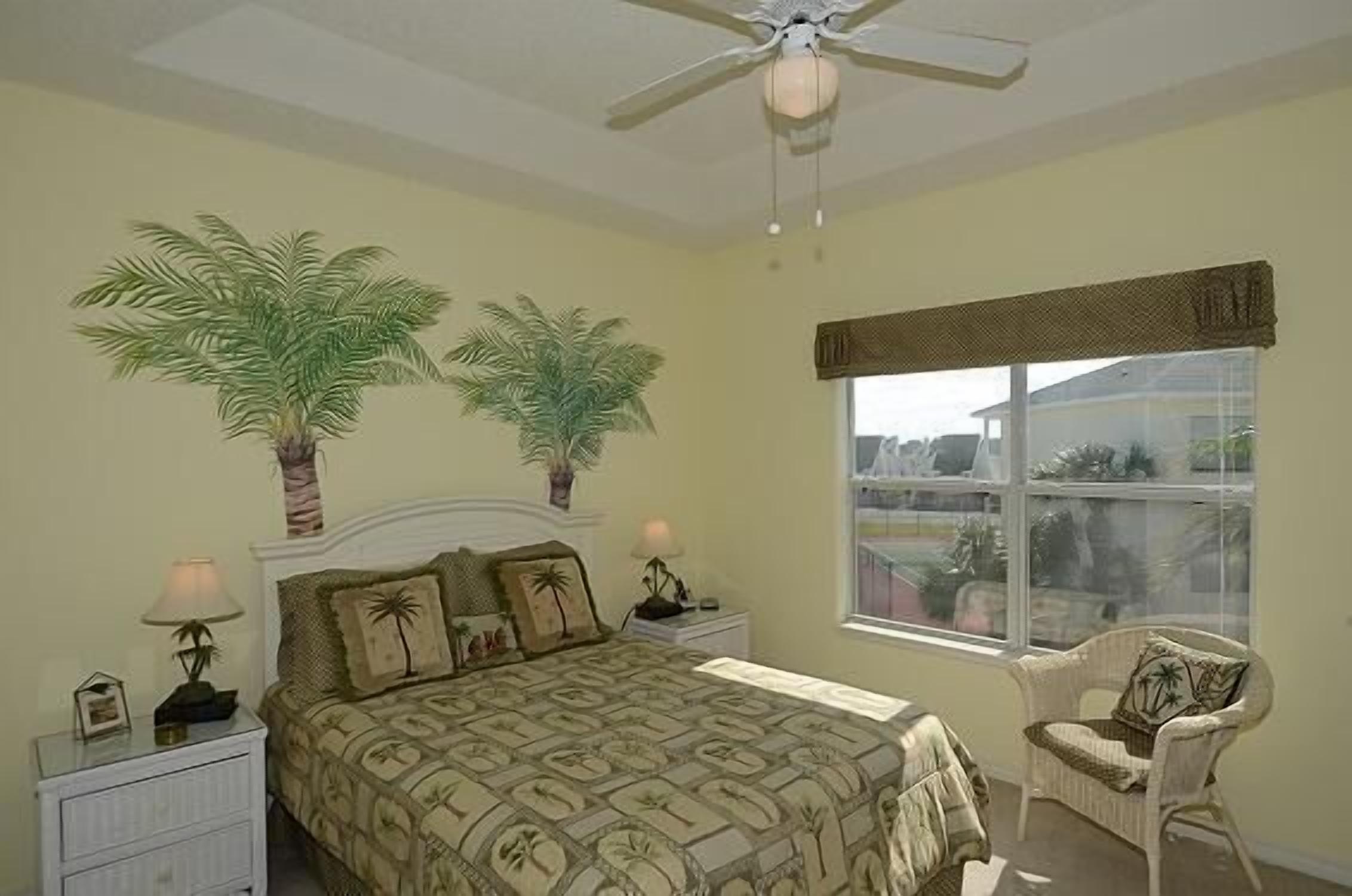 A bedroom with a bed, two nightstands, a chair, a ceiling fan, and a window with a view.