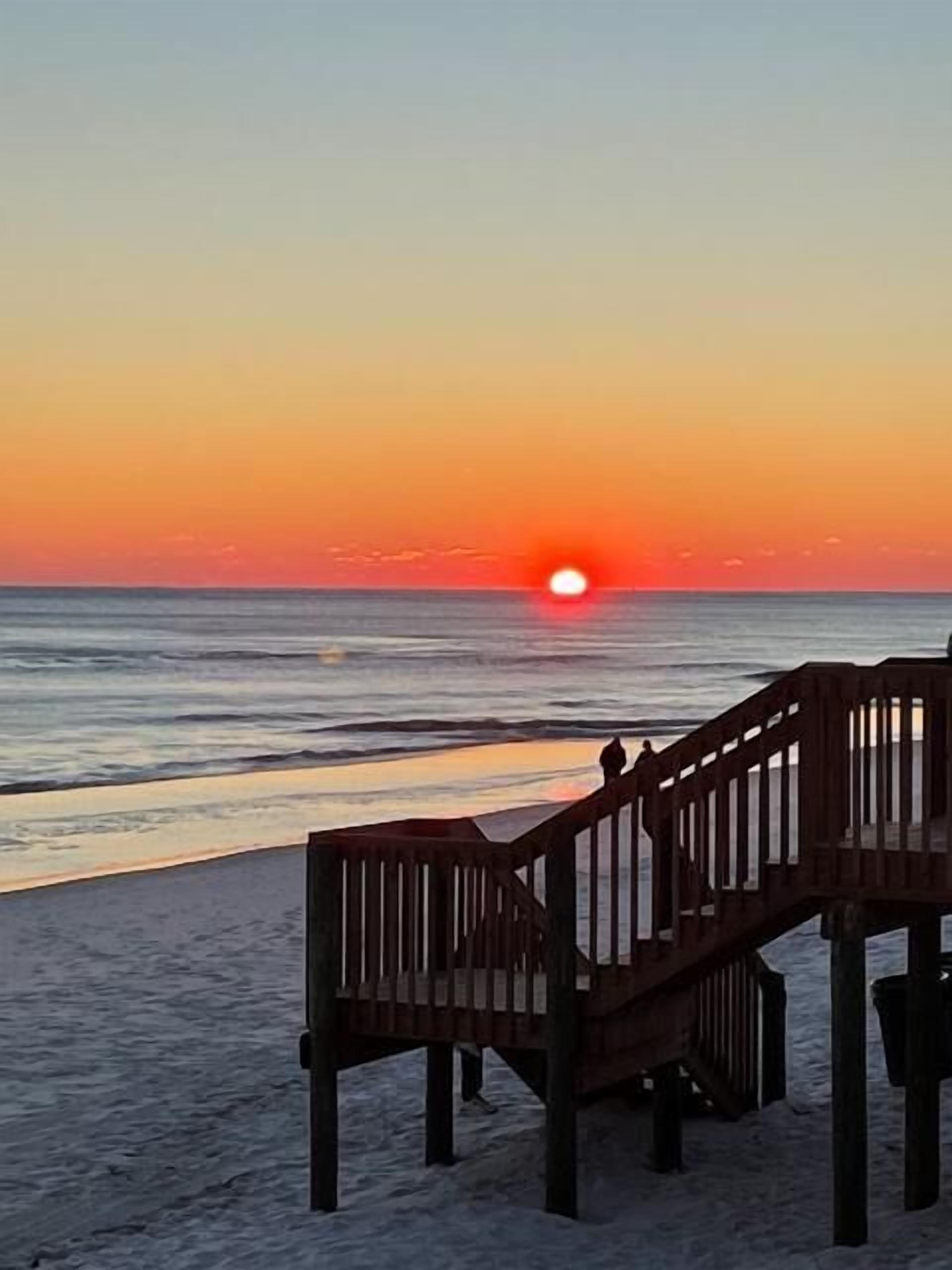 Une jetée en bois s’étendant sur une mer calme au coucher du soleil.
