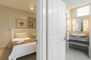 A hotel room with a bed, a nightstand, a lamp, and a bathroom with a sink and mirror. - Breakers Resort by Top Destinations (Umhlanga)