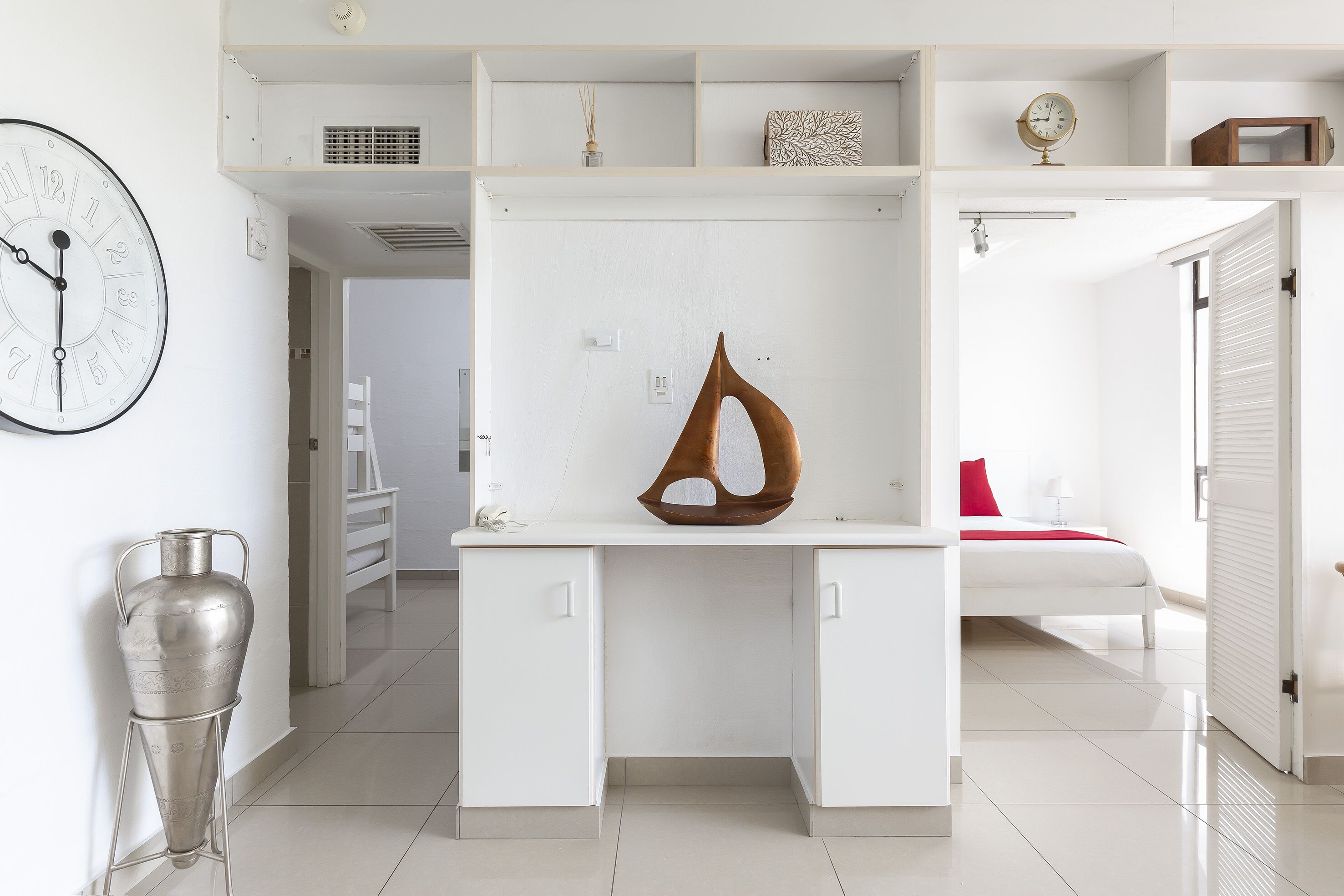Een moderne, goed verlichte kamer met een wit bureau, een grote klok en een decoratief beeldhouwwerk.