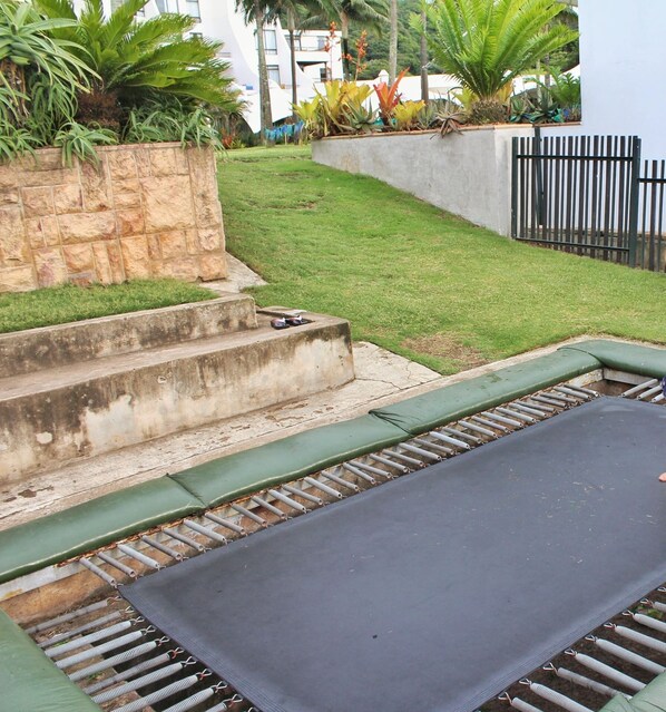 A concrete staircase leading up to a grassy area with a trampoline and a metal fence.