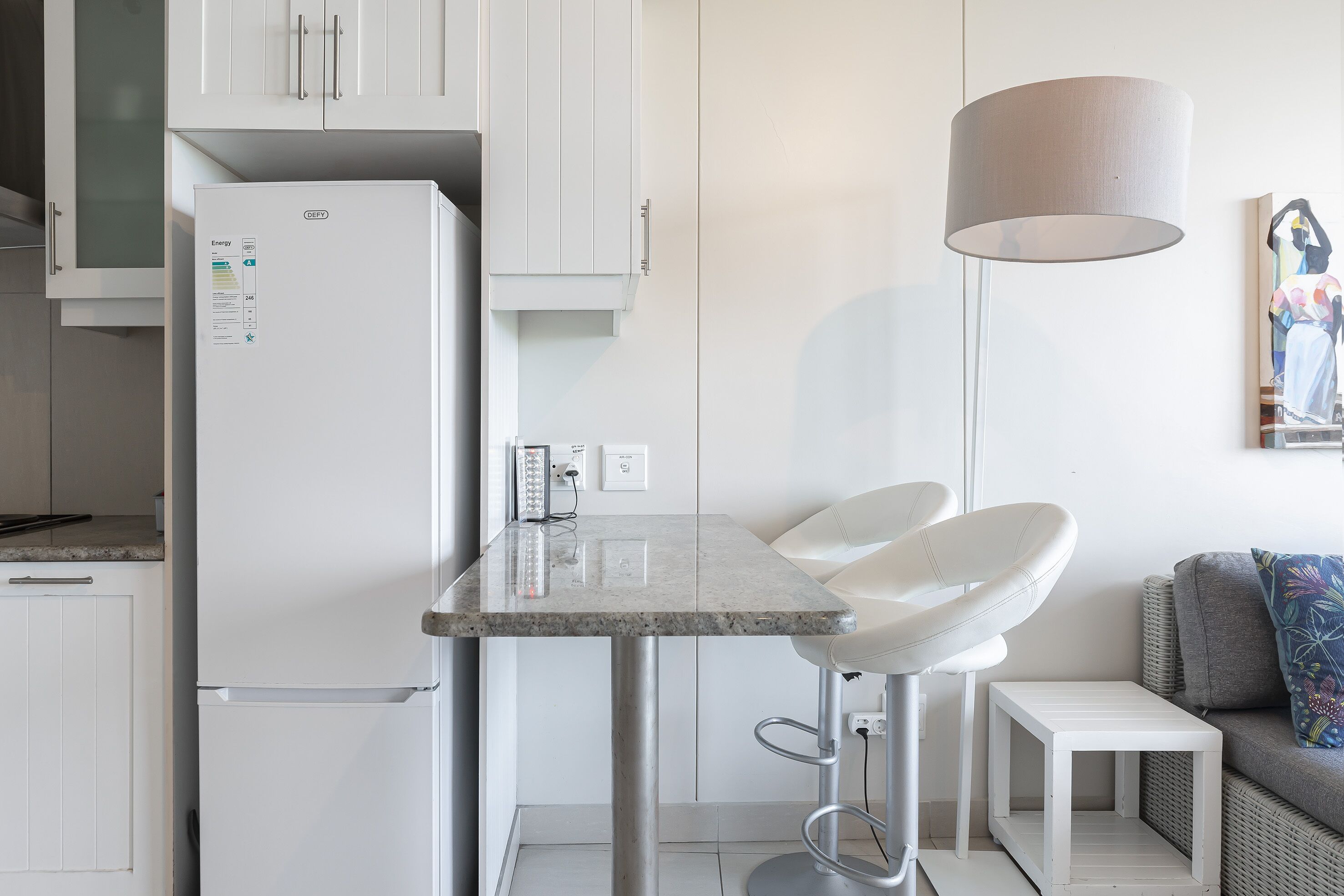 A modern kitchen with white cabinetry, a built-in refrigerator, a marble countertop, and a bar stool.