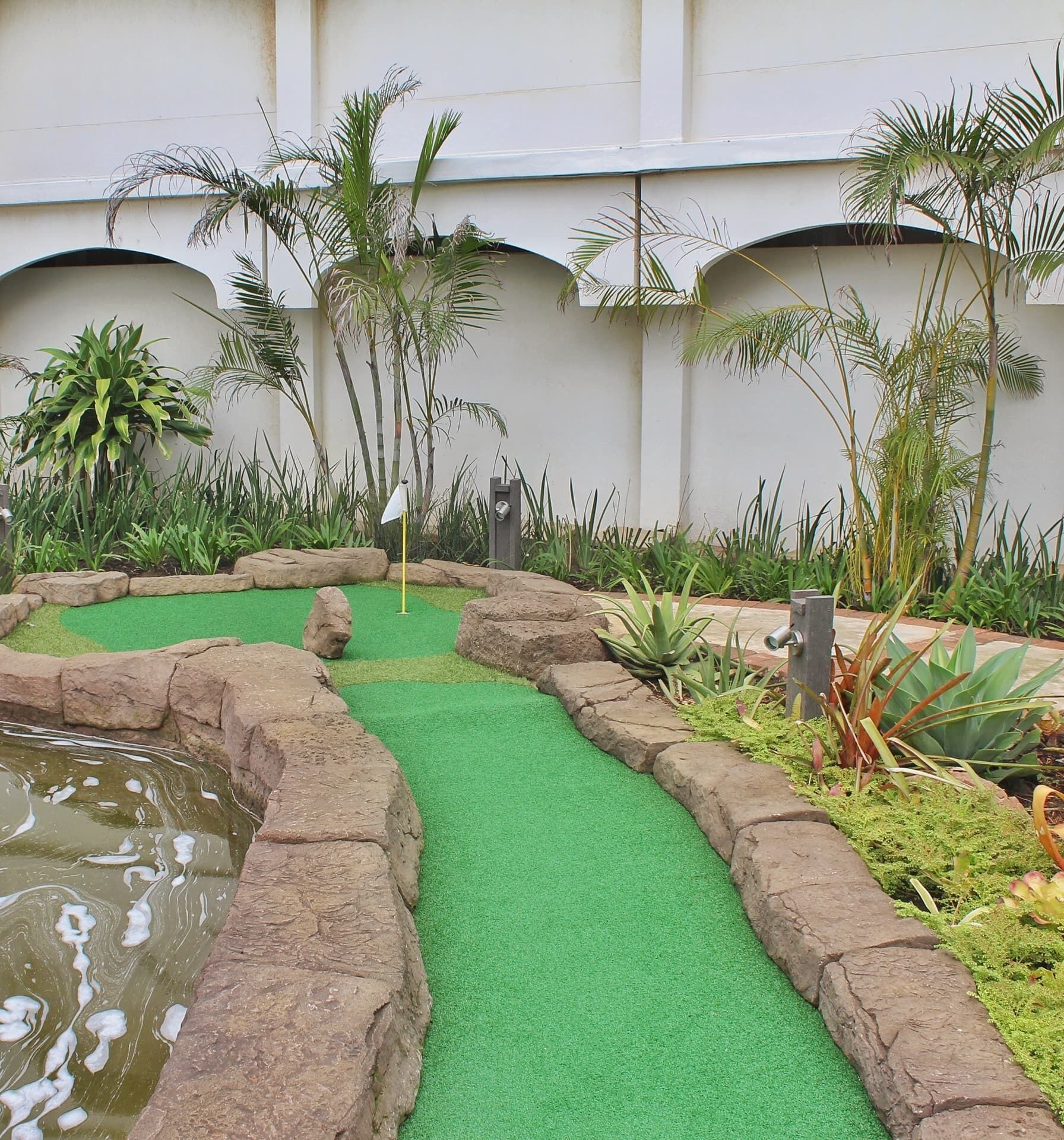 Ein Minigolfplatz mit grünem Kunstrasen, Felsenkanten und einem kleinen Teich.