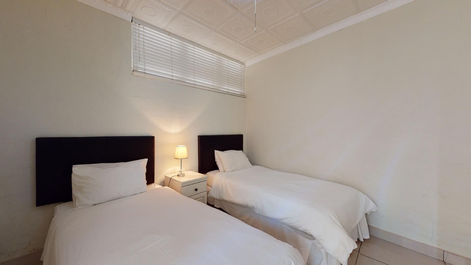 A hotel room with two beds, a nightstand with a lamp, and a window with blinds.