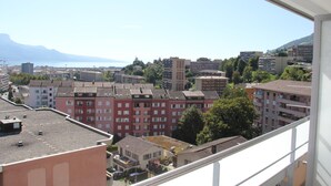 A high-rise building with multiple balconies, a view of a cityscape with various buildings, and a distant mountain range. - Hotel Abaca (Vevey)