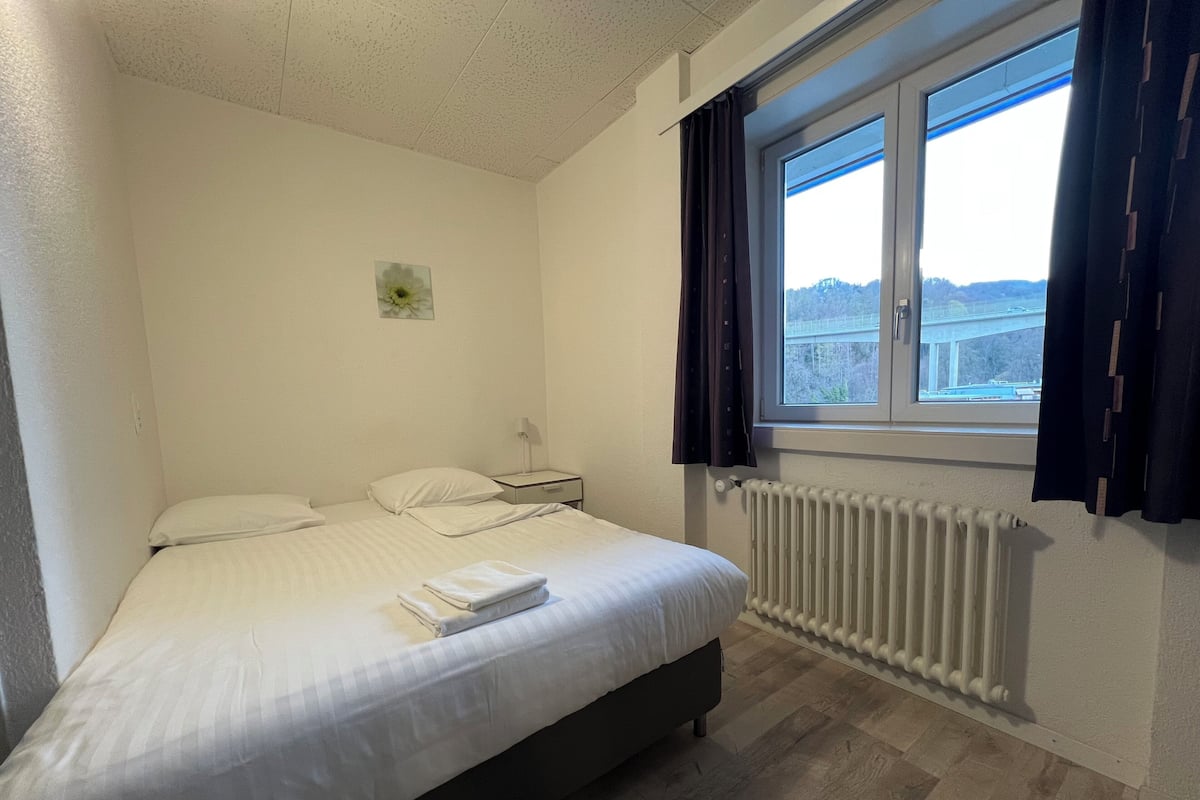 Un dormitorio con cama, mesita de noche, ventana con cortinas y radiador.