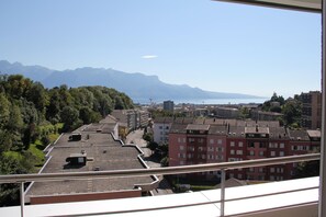 Vista desde un balcón que domina un paisaje urbano con edificios, cielo despejado y montañas distantes.