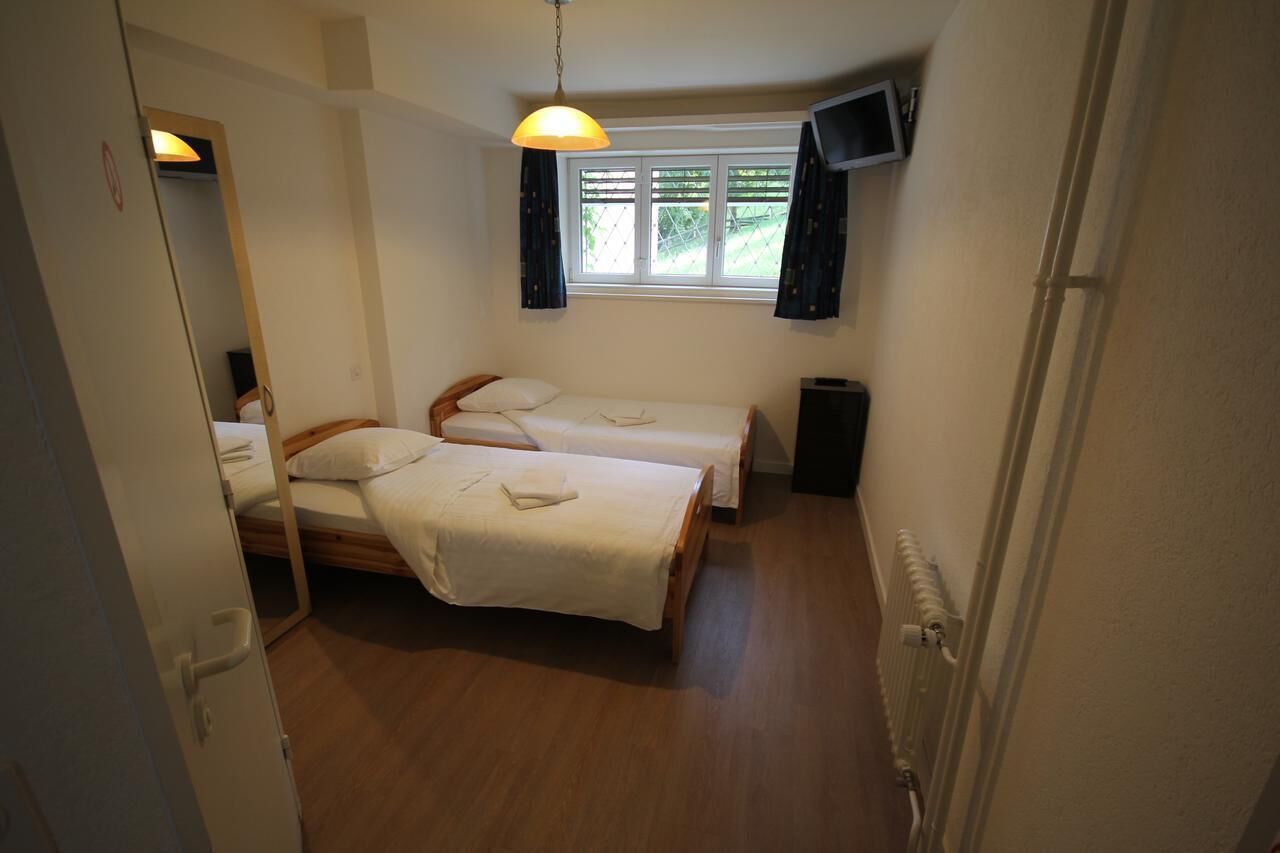 A small, clean room with two single beds, a TV, and a window with curtains.