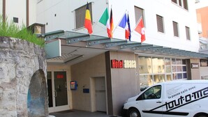 A hotel entrance with a sign reading "Hotel Abaca," a white van parked in front, and multiple flags hanging above. - Hotel Abaca (Vevey)