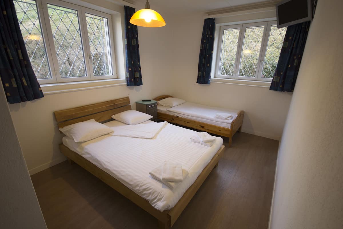 Un dormitorio con dos camas individuales, cabecero de madera, una mesita de noche, una lámpara y un televisor en la pared.