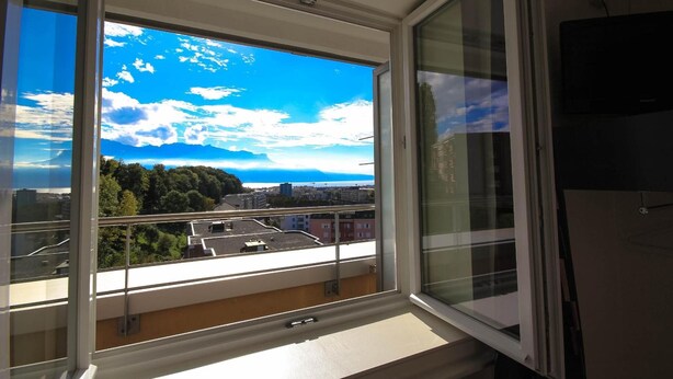 A room with a large window offering a view of a cityscape and greenery. - Hotel Abaca (Vevey)
