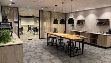 Habitación de hotel moderna con escritorio de madera, taburetes de bar, una zona de cocina y una sala de conferencias al fondo.