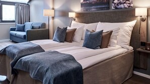 A modern hotel room with a large bed, a sofa, two bedside tables, and a window with curtains.