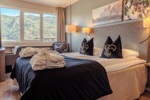 A hotel room with a bed, a chair, a desk, and a window with a mountain view.