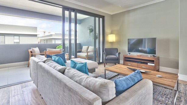 Una sala moderna con un sofá, sillones, un televisor y una mesa de centro de madera.