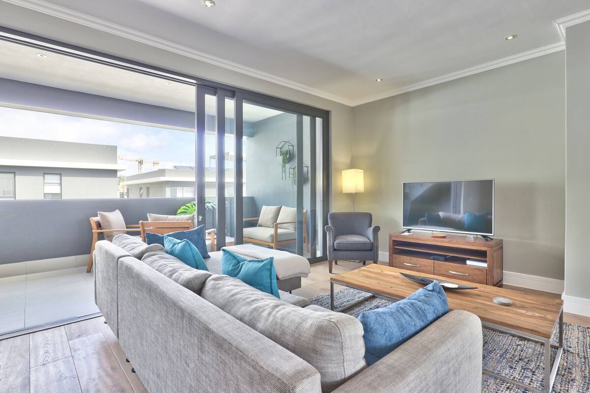 A modern living room with a sofa, armchairs, a TV, and a wooden coffee table.