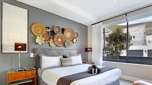 Un dormitorio moderno con una cama grande, una mesita de noche, una lámpara de pared y vistas al exterior a través de un ventanal amplio.