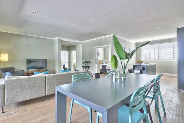 Un salon moderne avec un canapé gris, des fauteuils turquoise, une table à manger et un téléviseur.