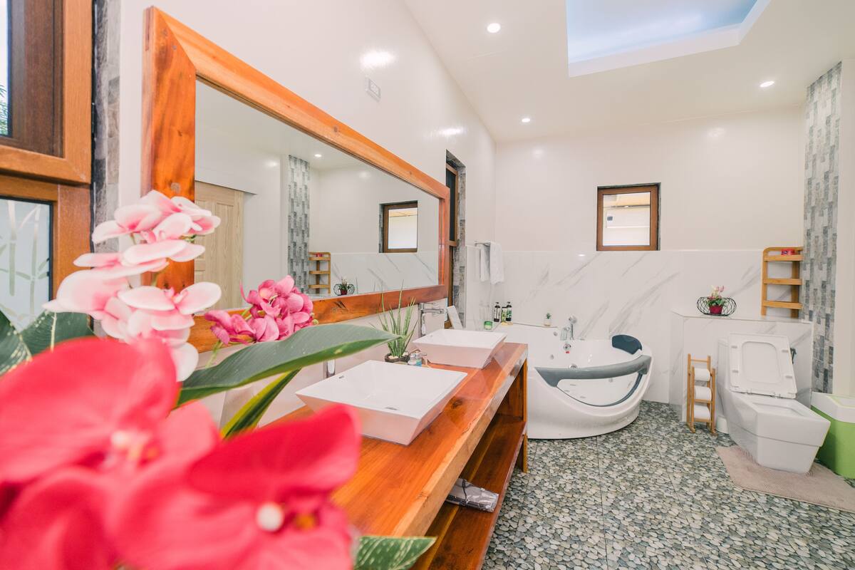 A modern bathroom with a wooden vanity, a large mirror, a freestanding bathtub, and a toilet.