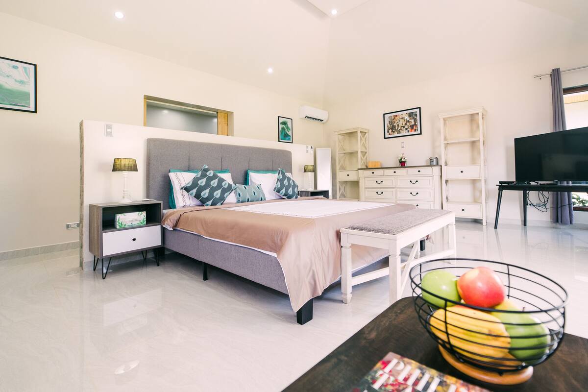 A modern bedroom with a bed, bedside tables, a TV, and a fruit bowl.