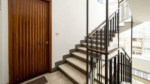 A wooden door, a staircase with black railings, and a view of buildings through large windows.
